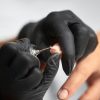 Close-up of manicurist hands removing cuticle with nail clippers from client fingernails.